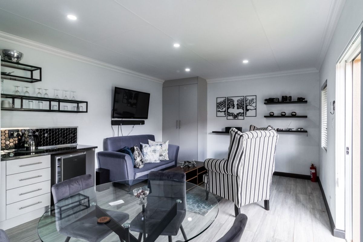 Modern open-plan living area featuring a compact kitchenette with built-in cabinetry, laminate flooring, and recessed lighting, leading to a bright outdoor access point.