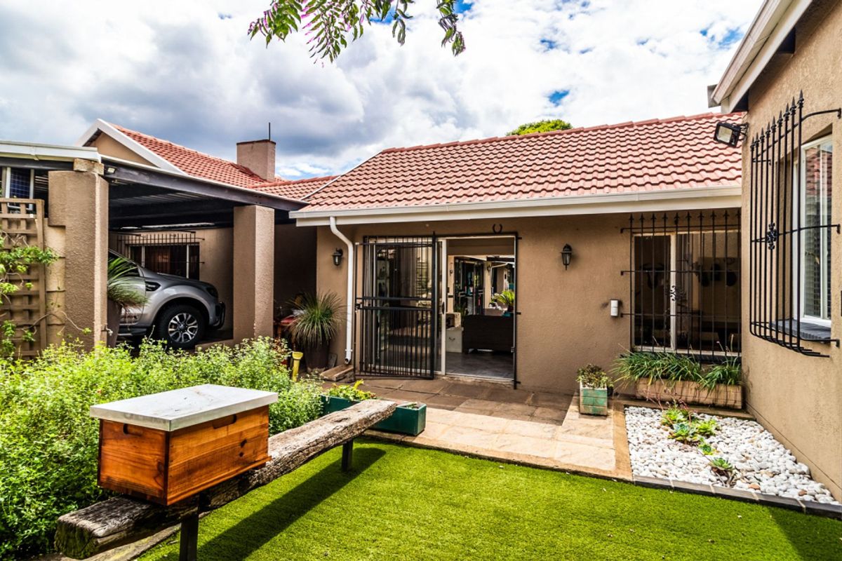A well-maintained rear exterior view featuring a paved patio area, artificial lawn, and a covered carport attached to the main dwelling.
