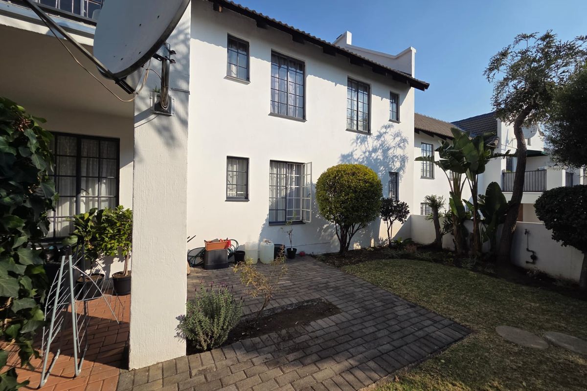 Rear view of the apartment featuring a paved patio area, small private garden, and white exterior facade with steel-framed windows.