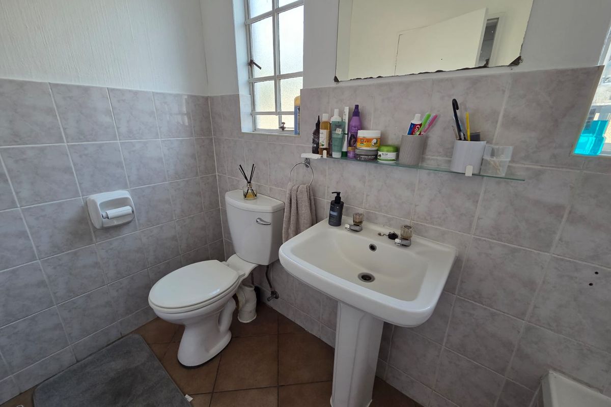 A functional bathroom featuring a pedestal washbasin, ceramic toilet, and tiled wall finishes with a window for natural light.