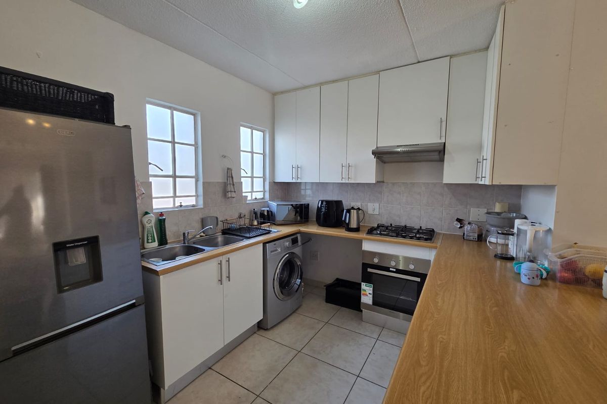 Functional kitchen featuring white cabinetry, laminate countertops, built-in oven, gas hob, and tiled flooring with integrated space for laundry appliances.