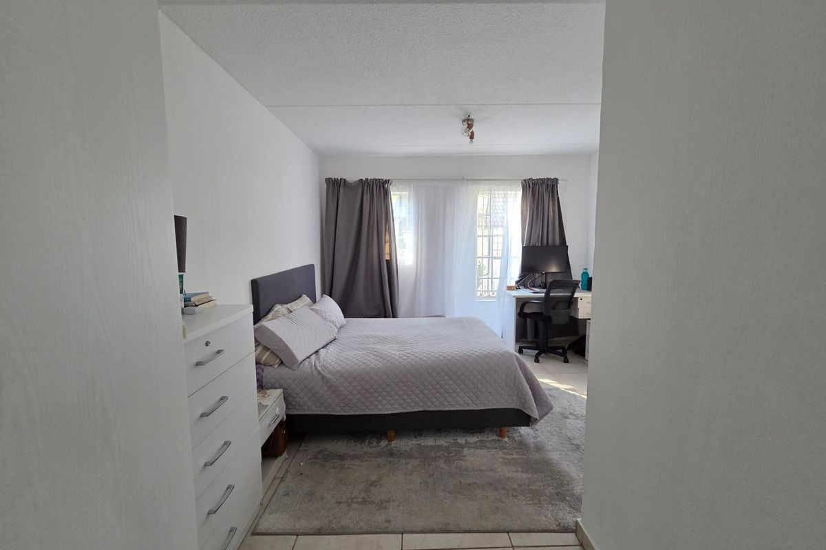 A functional bedroom featuring tiled flooring and a window fitted with security bars, providing natural light and a secure environment.