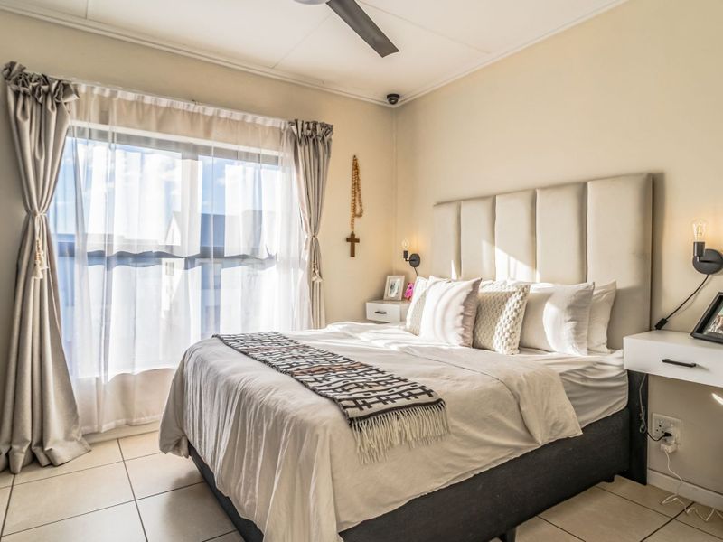 A well-maintained bedroom featuring tiled flooring, a ceiling fan, built-in wardrobe, and wall-mounted lighting fixtures.