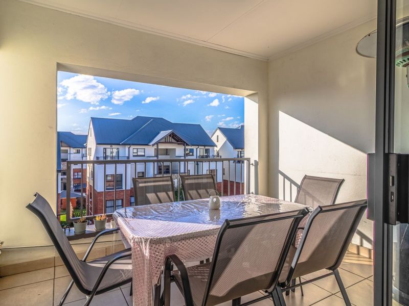 A covered balcony featuring tiled flooring and a metal balustrade, offering an outdoor space with views of the surrounding apartment complex.