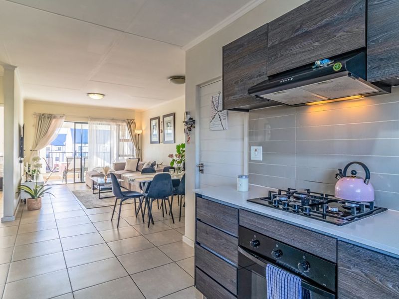 Open-plan living area featuring a modern kitchen with dark wood cabinetry, gas hob, and tiled flooring, flowing into a bright lounge with balcony access.