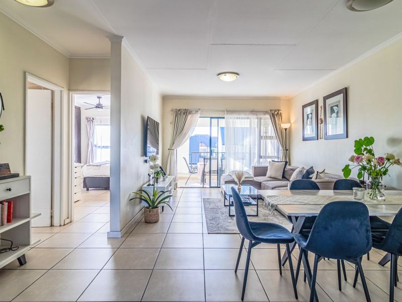 Spacious open-plan living and dining area featuring tiled flooring, neutral walls, and a sliding glass door leading to an outdoor balcony.