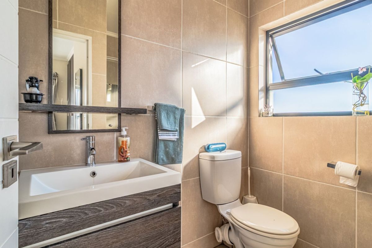 A modern, well-maintained bathroom featuring neutral wall tiles, a contemporary vanity with a basin, and a functional awning window for natural light.