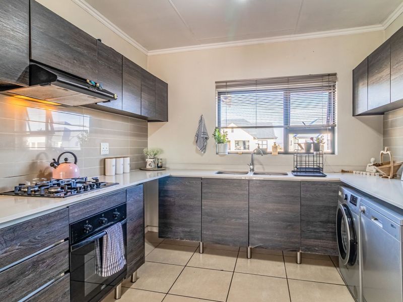 Modern kitchen featuring dark wood-grain cabinetry, stone-look countertops, gas hob, built-in oven, and integrated laundry plumbing.