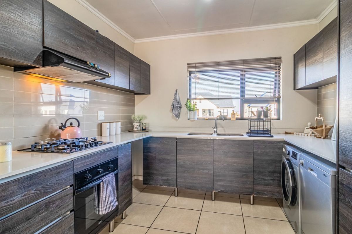 Modern kitchen featuring dark wood-grain cabinetry, stone-look countertops, gas hob, built-in oven, and integrated laundry plumbing.