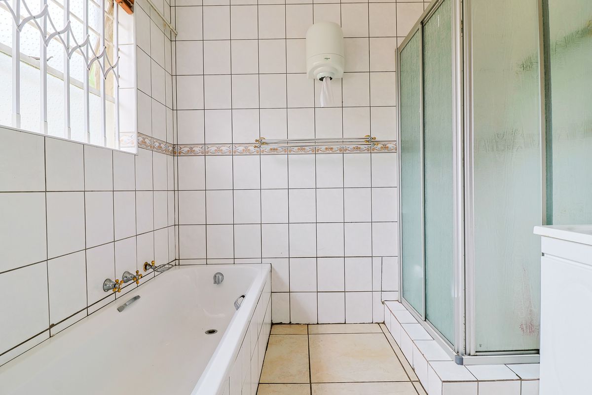 A functional bathroom featuring a bathtub, separate shower enclosure, and white wall tiling. The space is clean but dated in its finishes.