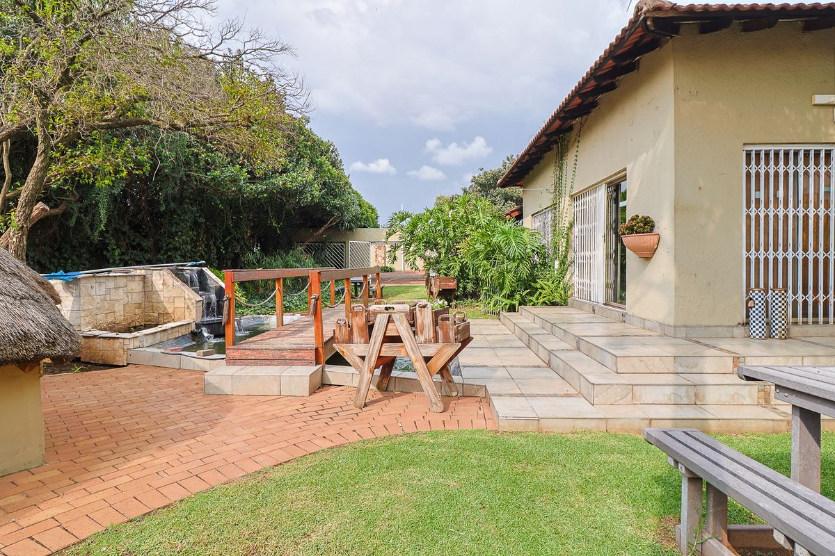 Rear exterior view featuring a tiled patio, brick paved garden area, water feature with a wooden bridge, and direct access to the home.