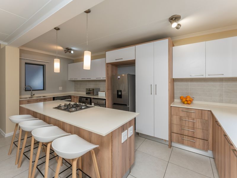 Modern kitchen featuring a central island with a gas hob, stone countertops, ample built-in cabinetry, and neutral tiled flooring.