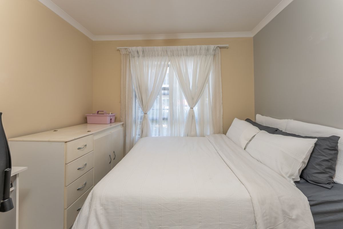 A functional bedroom featuring neutral wall tones, coving, and a window with sheer curtains, providing a comfortable and well-lit sleeping space.