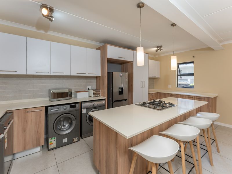 Modern kitchen featuring wood-tone and white cabinetry, stone countertops, a central island with a gas hob, and integrated appliances.