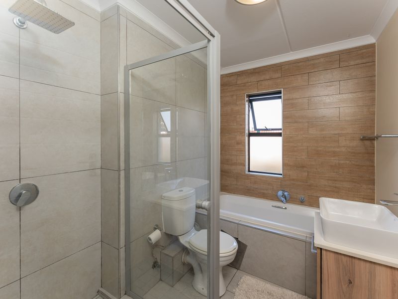 Modern bathroom featuring a glass-enclosed shower, bathtub, vanity basin, and contemporary neutral and wood-look wall tiling.