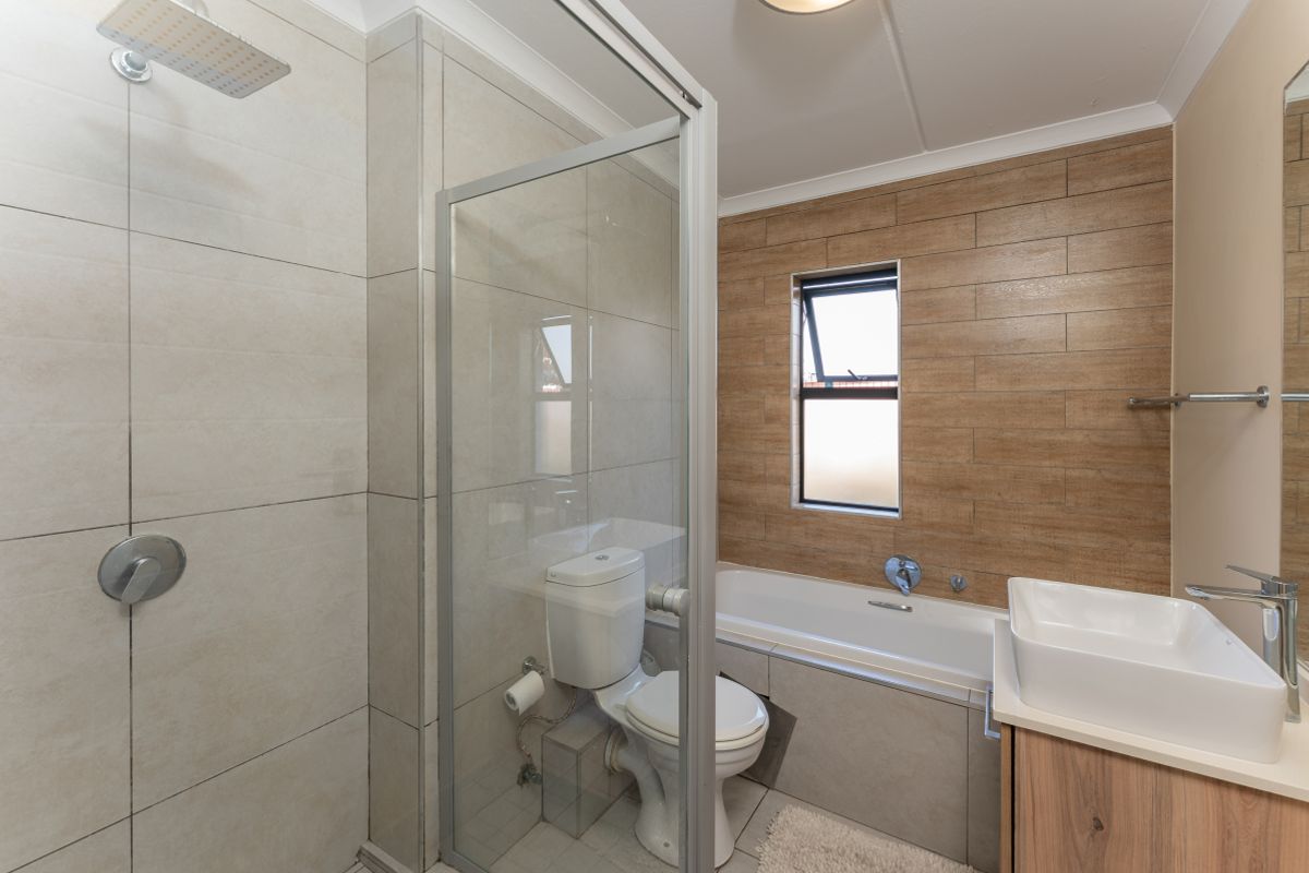 Modern bathroom featuring a glass-enclosed shower, bathtub, vanity basin, and contemporary neutral and wood-look wall tiling.