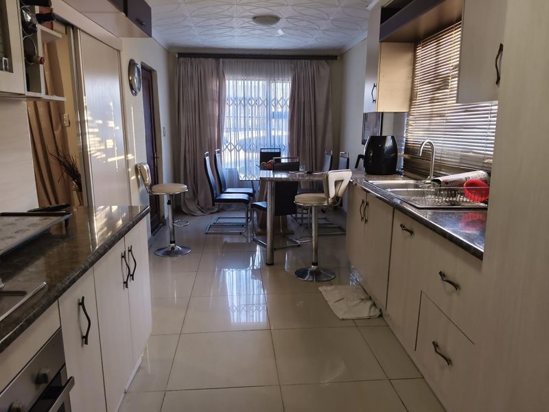 Open-plan kitchen and dining area featuring tiled flooring, built-in cabinetry with granite countertops, and natural light through large window treatments.