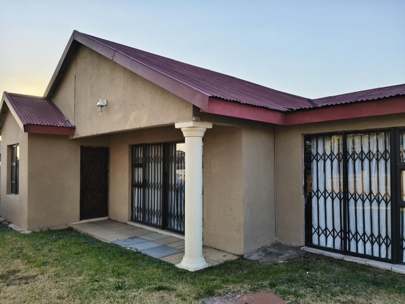 Rear exterior view of the house featuring a covered patio area, sliding glass doors with security gates, and a corrugated metal roof.