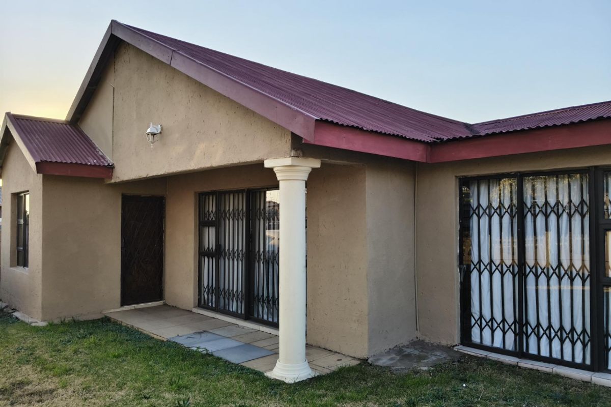 Rear exterior view of the house featuring a covered patio area, sliding glass doors with security gates, and a corrugated metal roof.