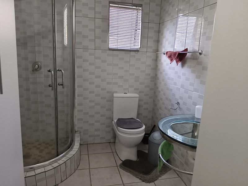 A functional bathroom featuring a glass shower enclosure, a modern glass vessel sink, and neutral wall tiling.