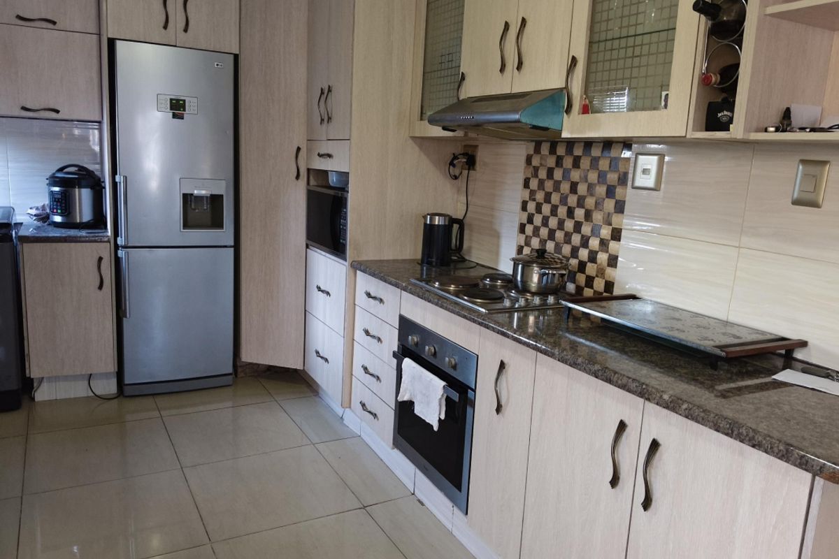 A functional kitchen featuring light wood-grain cabinetry, granite countertops, a mosaic tile backsplash, and integrated appliances including an oven and hob.