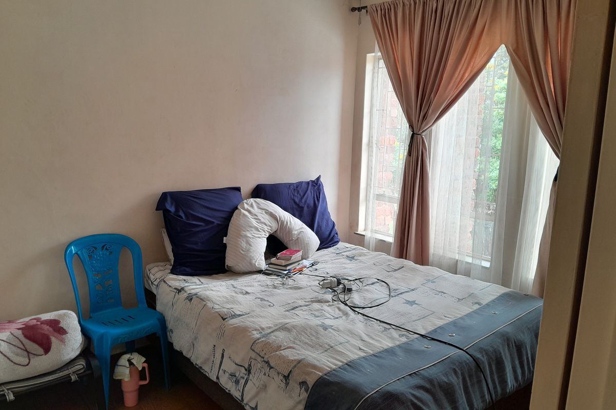 A standard bedroom featuring tiled flooring and large windows with installed curtain rails, providing natural light to the space.