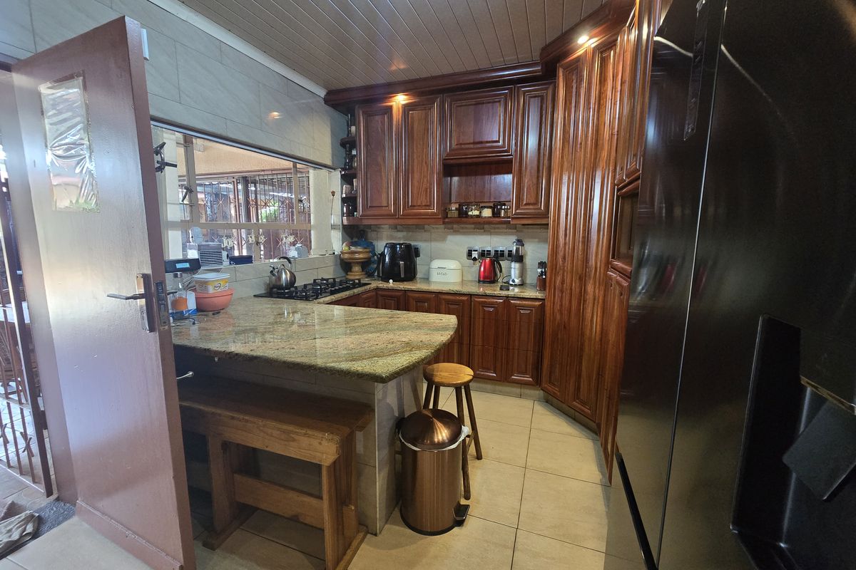 A functional kitchen featuring warm wooden cabinetry, granite countertops, a gas hob, and tiled flooring with a classic tongue and groove ceiling finish.