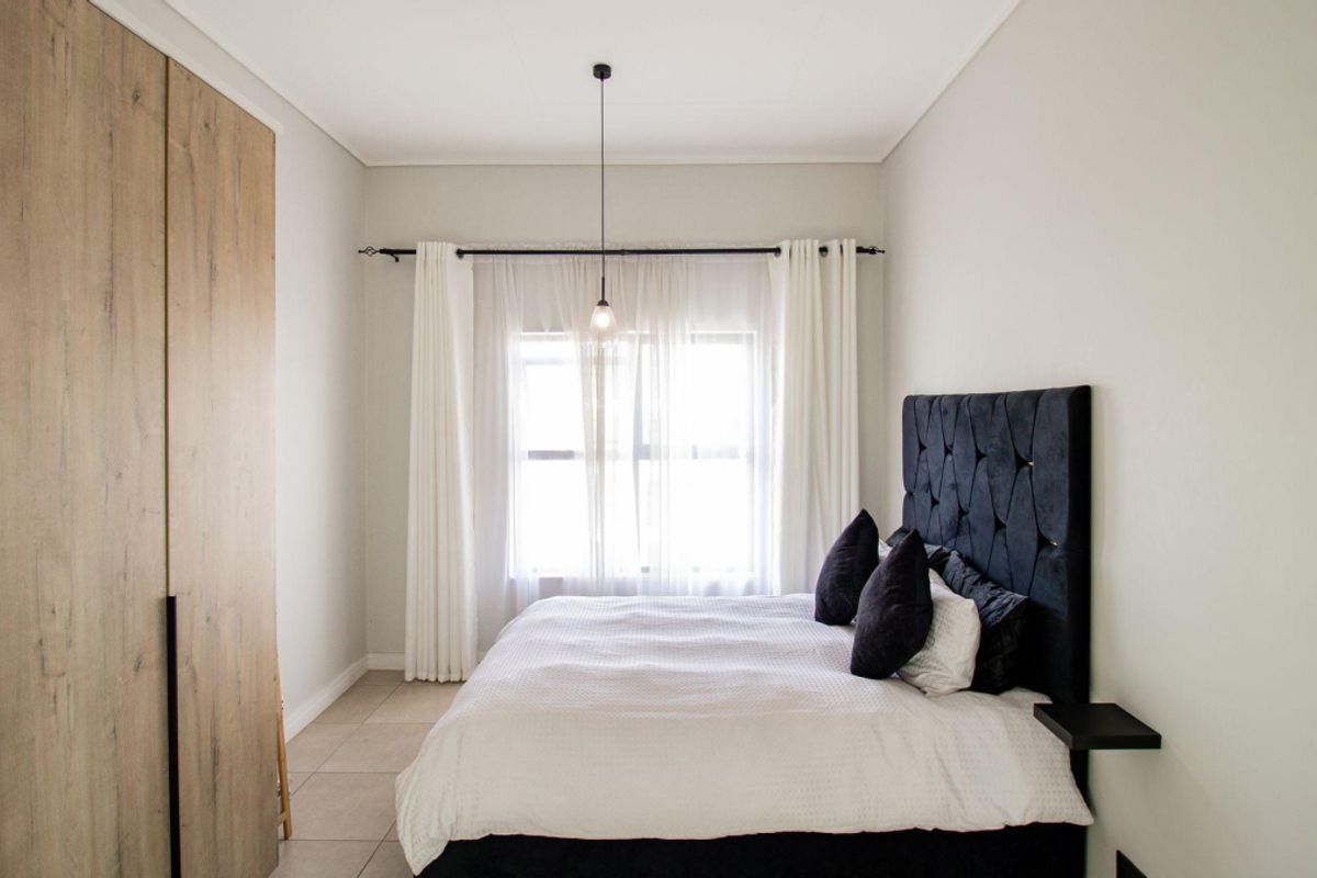 A well-maintained bedroom featuring neutral tiled flooring, a large built-in wardrobe with wood-grain finish, and a central pendant light fixture.