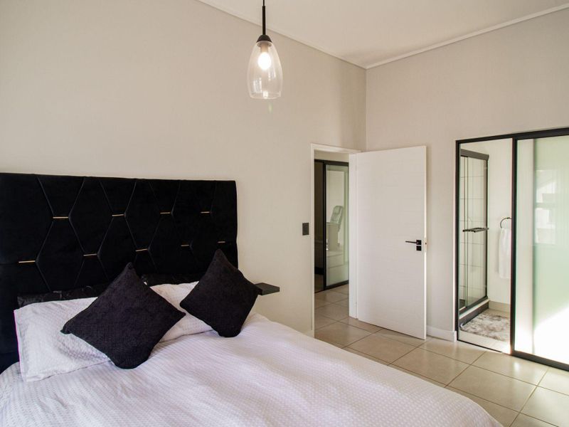 Modern bedroom featuring neutral tiled flooring, a contemporary pendant light, and direct access to an en-suite bathroom through a sliding glass door.