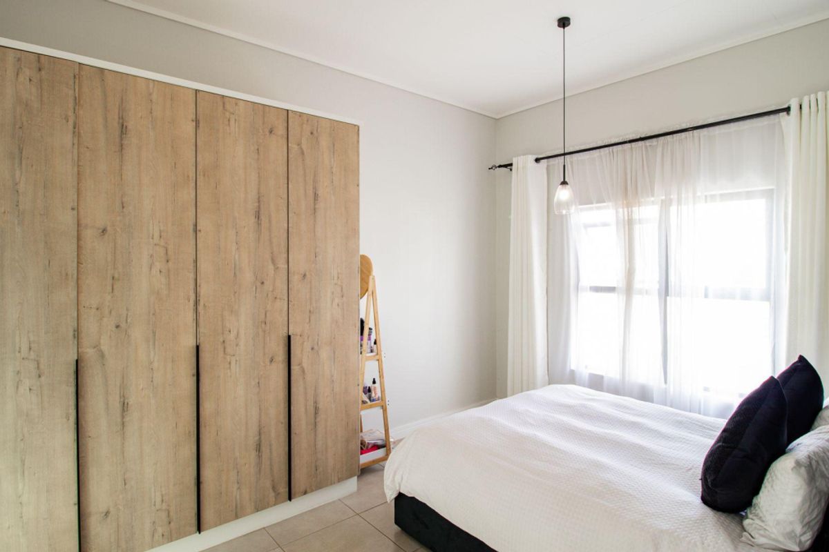A well-maintained bedroom featuring light wood-finish built-in wardrobes, neutral tiled flooring, and a modern pendant light fixture.