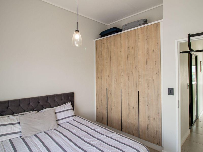 A well-maintained bedroom featuring modern wood-finish built-in wardrobes, neutral wall tones, and tiled flooring with a view into the adjacent hallway.
