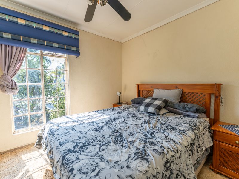 A bedroom featuring a ceiling fan, carpeted flooring, and a large grid-pattern window allowing natural light.