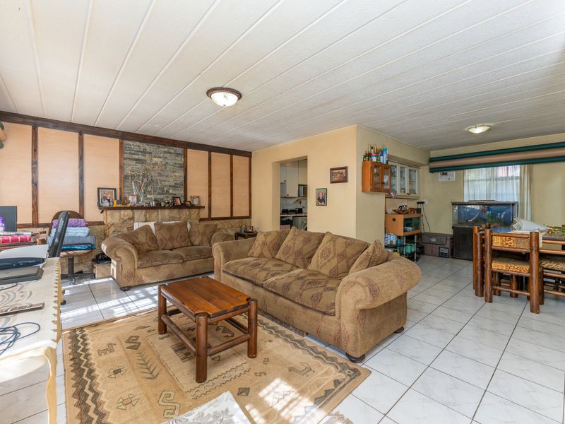 Spacious open-plan living area featuring tiled floors, a stone fireplace, and direct access to a kitchen space.