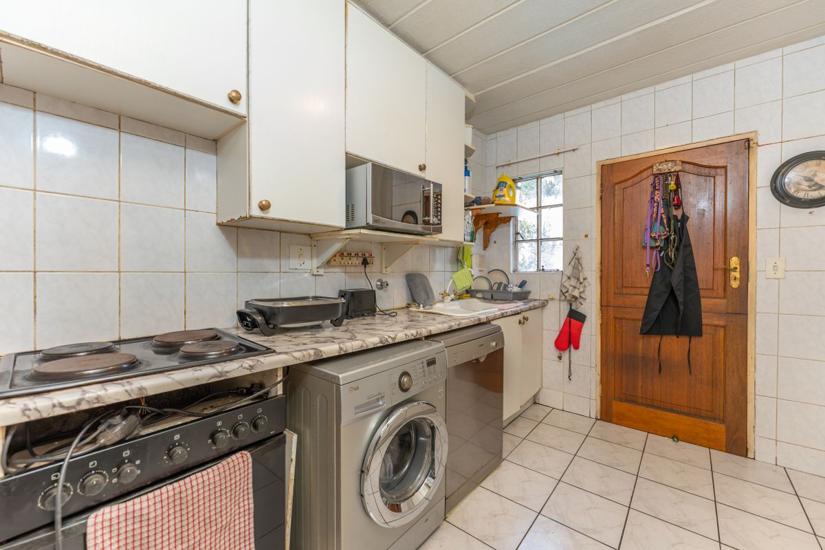 A functional kitchen featuring built-in cabinetry, a laminate countertop, an electric hob, and tiled finishes, providing a practical workspace with direct access to an exterior door.