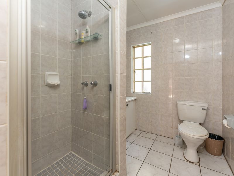 A functional bathroom featuring a glass-enclosed shower, toilet, and tiled finishes throughout, offering a clean and practical layout.