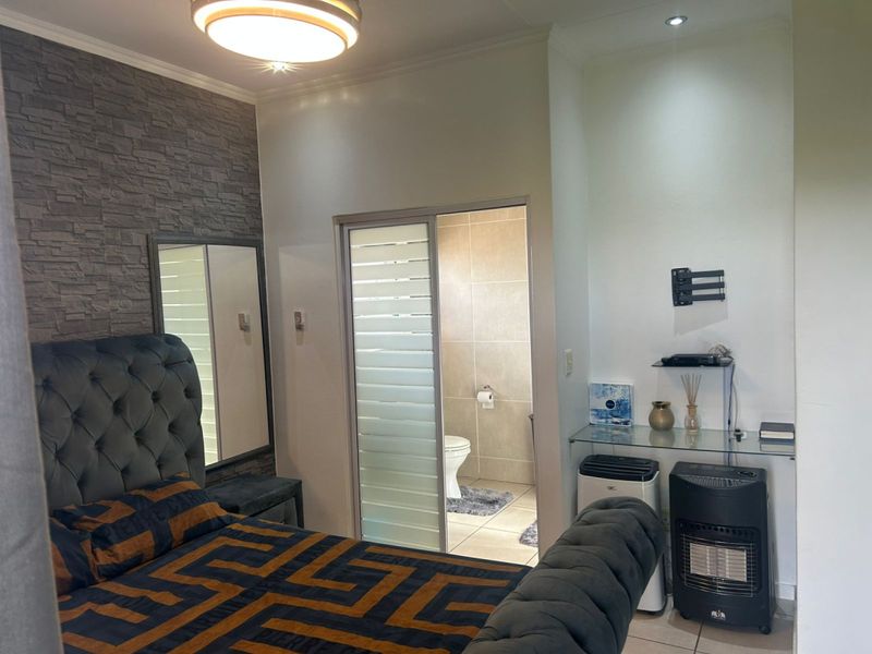 A well-maintained bedroom featuring a stone veneer accent wall, recessed lighting, and an en-suite bathroom accessed via a sliding door.