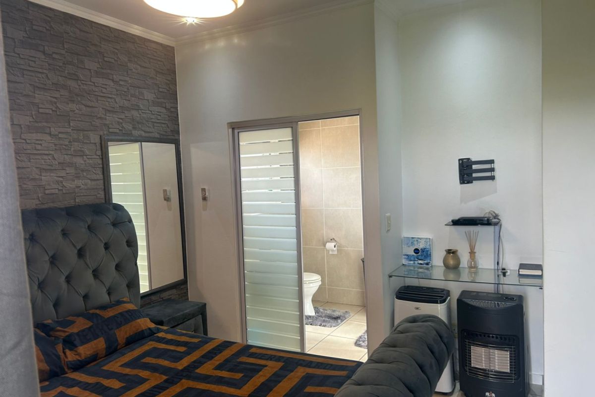 A well-maintained bedroom featuring a stone veneer accent wall, recessed lighting, and an en-suite bathroom accessed via a sliding door.