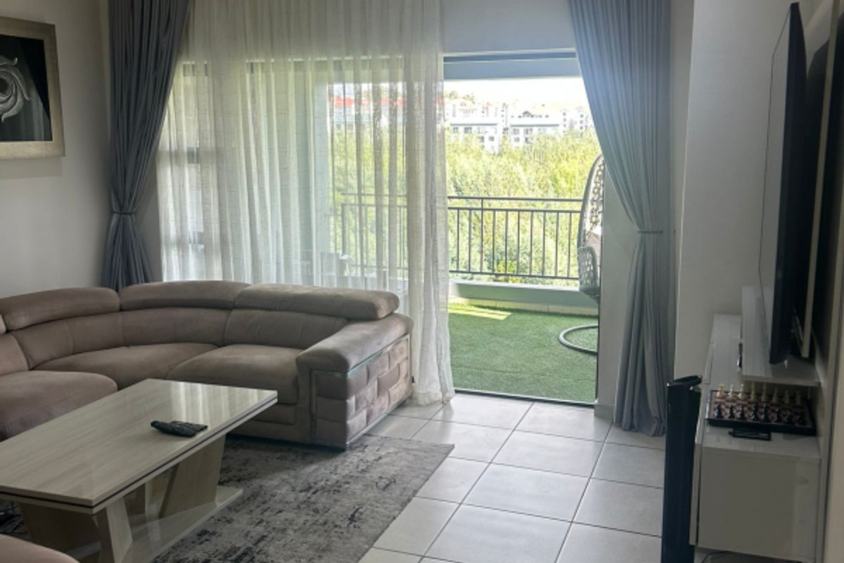 A bright living room featuring large format floor tiles, recessed lighting, and a sliding glass door providing direct access to a private balcony.
