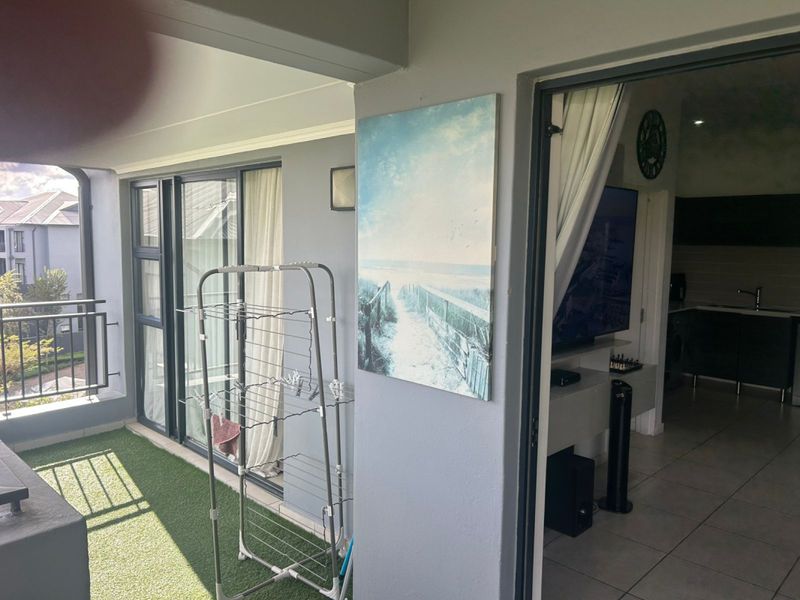 A covered balcony featuring artificial grass flooring and sliding glass doors providing access to the interior living space.