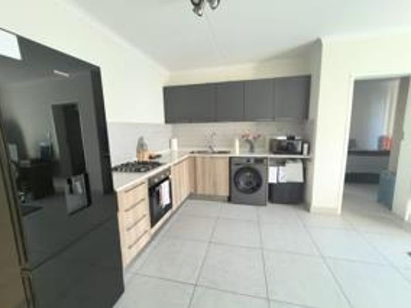 Modern kitchen featuring light wood-tone lower cabinetry, dark upper cabinets, gas hob, built-in oven, and integrated laundry appliance with tiled flooring.
