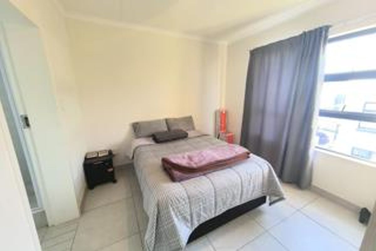 A functional bedroom featuring tiled flooring and a large window with curtain tracks, providing natural light and a neutral base for personalization.