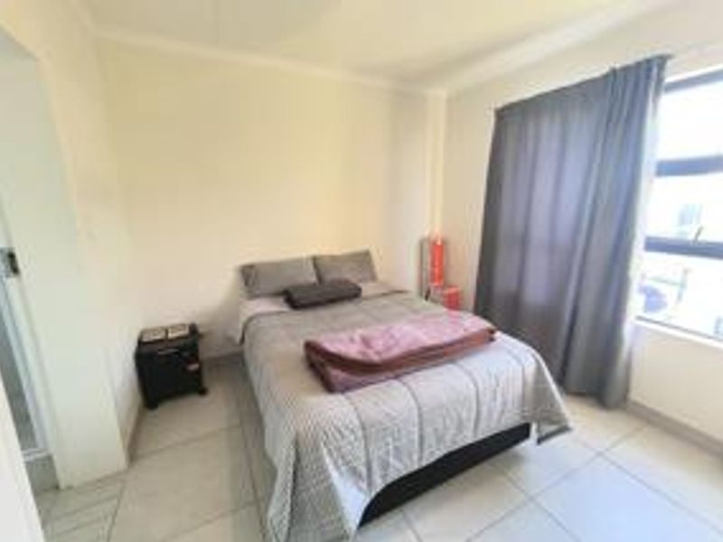 A functional bedroom featuring tiled flooring and a large window with curtain tracks, providing natural light and a neutral base for personalization.