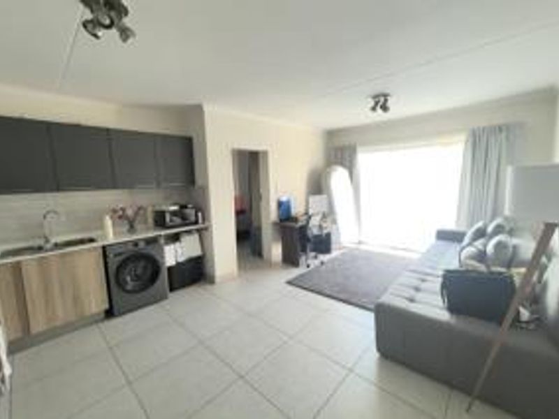 Open-plan living area featuring a modern kitchen with dark upper cabinets, light wood lower cabinets, tiled flooring, and direct access to a balcony.
