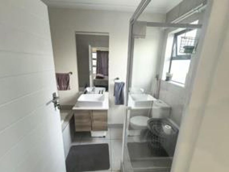 A functional bathroom featuring a modern vessel sink with vanity, a glass-enclosed shower, and a toilet, finished with neutral wall and floor tiles.
