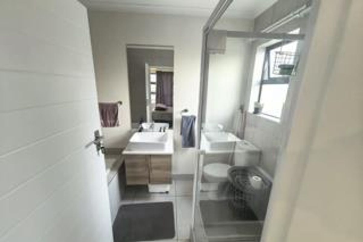 A functional bathroom featuring a modern vessel sink with vanity, a glass-enclosed shower, and a toilet, finished with neutral wall and floor tiles.