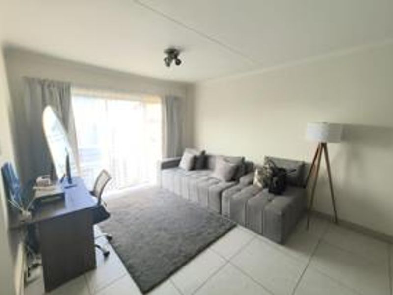 A bright living room featuring neutral tiled flooring and a large sliding glass door providing natural light and access to the exterior.