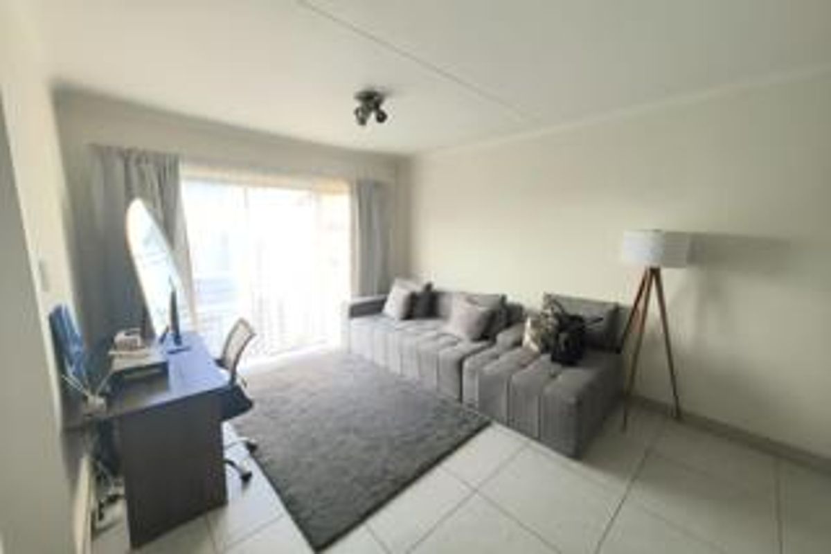 A bright living room featuring neutral tiled flooring and a large sliding glass door providing natural light and access to the exterior.