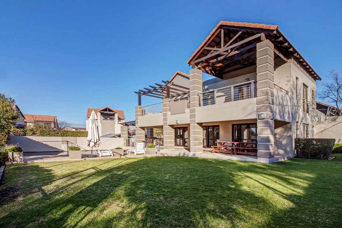 Rear view of a two-story apartment building featuring a spacious lawn, paved patio area, timber pergola, and a covered balcony with stone-clad pillars.