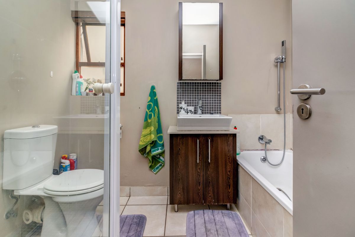 A functional bathroom featuring a vessel sink with vanity cabinet, a bathtub with shower mixer, and a wall-mounted mirror cabinet.
