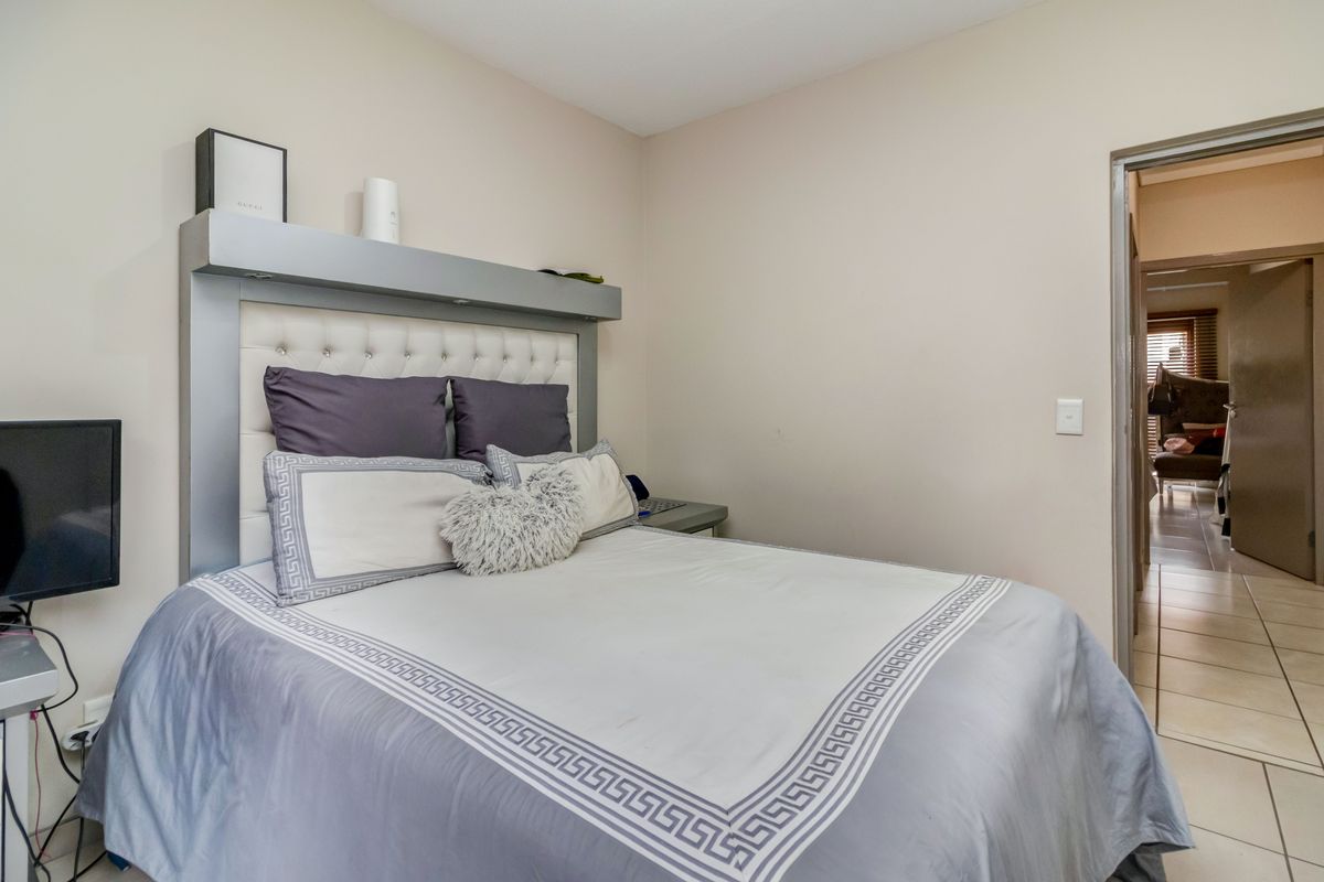 A bedroom featuring a built-in headboard and tiled flooring, with an adjacent hallway visible through the doorway.